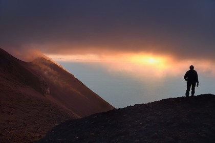 Italie, Sicile, iles Eoliennes, classées Patrimoine Mondial de l'UNESCO, ile de Stromboli, randonneur observant les fumerolles d'une éruption sur les pentes du volcan actif au coucher de soleil