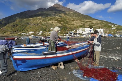 Italie, Sicile, iles Eoliennes, classées Patrimoine Mondial de l'UNESCO, ile de Stromboli, le pecheur Gaetano Cusolito réparant ses filets avec ses deux frères sur la plage de Scari et le volcan du Stromboli en arrière plan