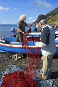 Italie, Sicile, iles Eoliennes, classées Patrimoine Mondial de l'UNESCO, ile de Stromboli, le pecheur Gaetano Cusolito réparant ses filets avec ses deux frères sur la plage de Scari et le volcan du Stromboli en arrière plan