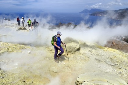 Italy, Sicily, Aeolian Islands, listed as World Heritage by UNESCO, Vulcano Island, hikers climbing the crater of volcano della Fossa through sulfur fumaroles, the island of Lipari then Salina island in the background
