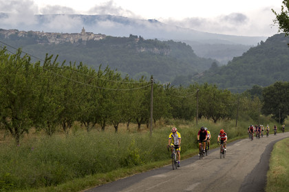 France, Vaucluse (84), Venasque, culture de l'amande par les Frères Silvain, paysans nougatiers, champ d'amandiers, cyclistes sur route et le village de Venasque en arrière plan