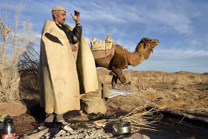 Iran, Isfahan province, Dasht-e Kavir desert, Mesr in Khur and Biabanak County, camel owner Ali Saraban wearing his grandfather camel wool felt (namad) and one of his camels at Kuh e-Sefid bivouac